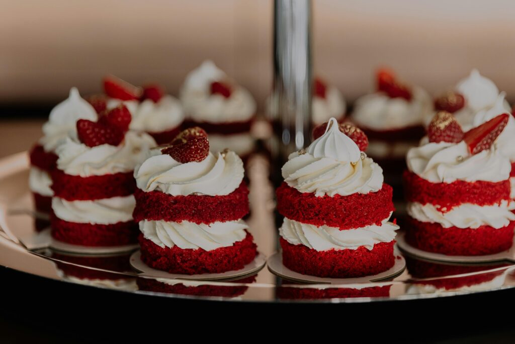 Close-up of red velvet mini cakes topped with whipped cream and strawberries on a tray.