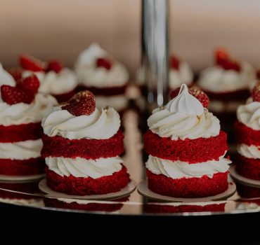 Close-up of red velvet mini cakes topped with whipped cream and strawberries on a tray.